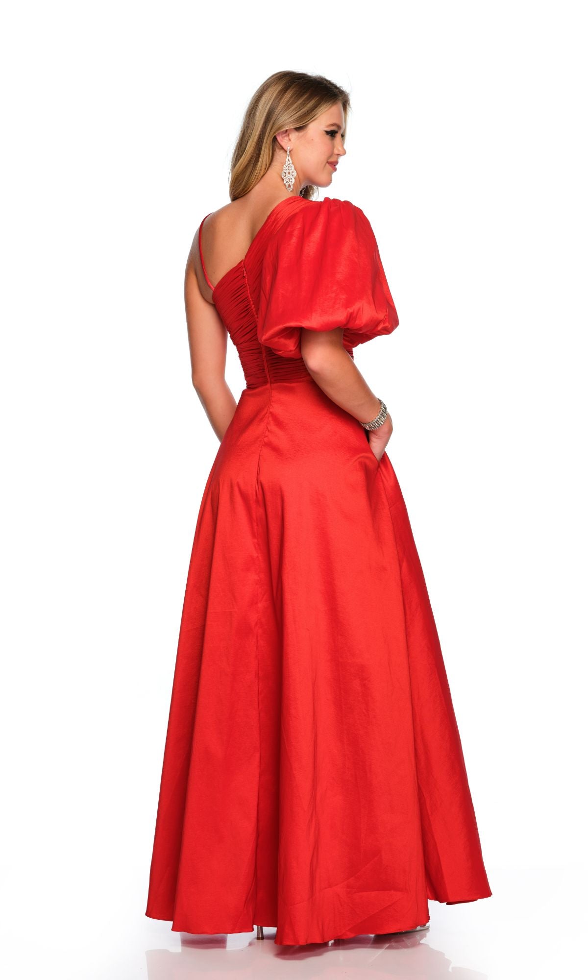 Woman in the Long Formal Dress 11577 by Dave and Johnny—a floor-length, bright red gown with puff sleeves and a fitted bodice—stands slightly turned with her back to a white background.
